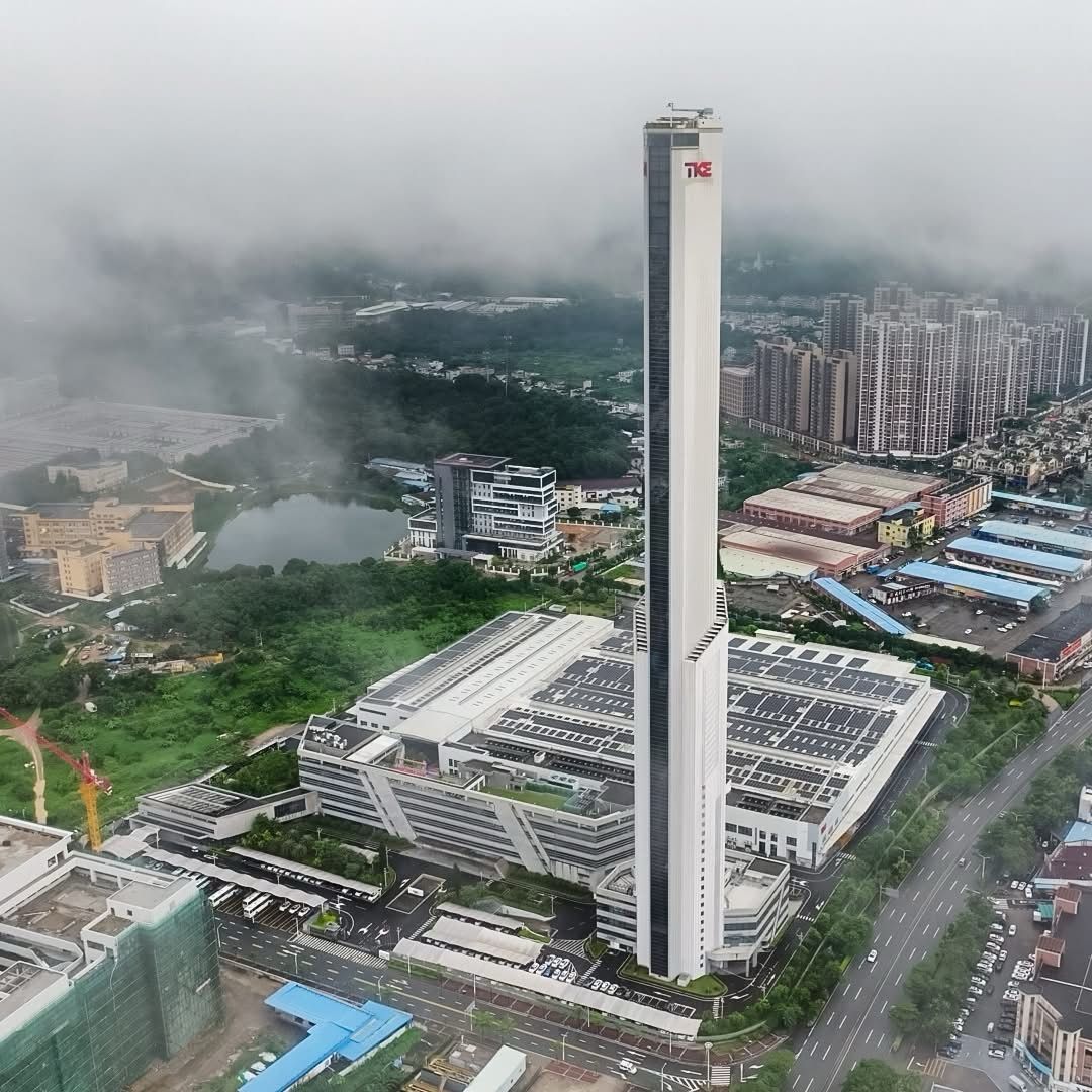 Aerial view of the 248-metre TKE Zhongshan test tower, a slender white spire rising above the manufacturing plant